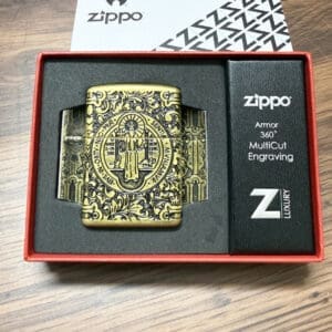 Brass Zippo lighter with ornate engraving in a black foam insert of a red gift box, showing circular crest and detailed scrollwork