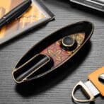 Premium black and gold cigar lighter with an ornate red-and-gold patterned insert, placed on a desk beside a pen and tools