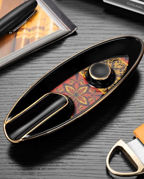 Premium black and gold cigar lighter with an ornate red-and-gold patterned insert, placed on a desk beside a pen and tools