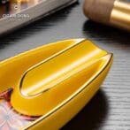 Close-up of a bright yellow, glossy cigar ashtray with a curved groove on a floral-pattern tray; CigarLoong logo visible in the corner.
