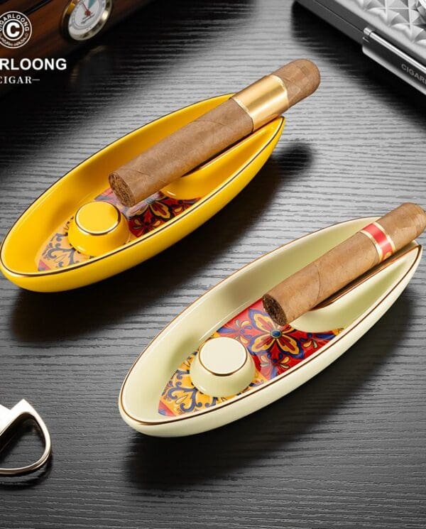 Two decorative boat-shaped cigar trays with colorful patterned interiors, each holding a cigar, visible with a lighter and accessories nearby; brand logo CIGARLOONG in the top left.