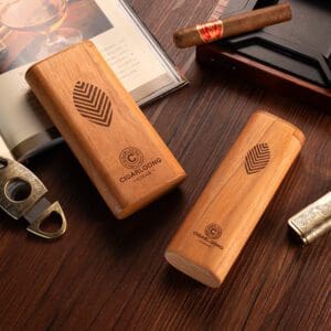 Two wooden cigar cases with leaf logo and brand name on a dark wooden table, accompanied by a cigar, lighter, and an open book/album nearby.