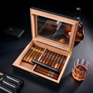 Open wooden cigar humidor showing a row of cigars, some with yellow bands, and a built-in humidifier; whiskey bottle and glass nearby.