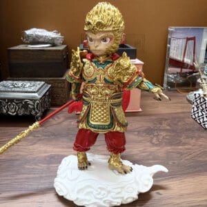 Gold-painted monkey-warrior figurine in ornate armor, standing on a white cloud pedestal and gripping a red staff.