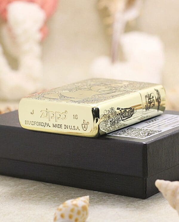 Gold Zippo lighter resting on a black gift box, with decorative engravings and text like 'Zippo' and 'Made in USA' visible.